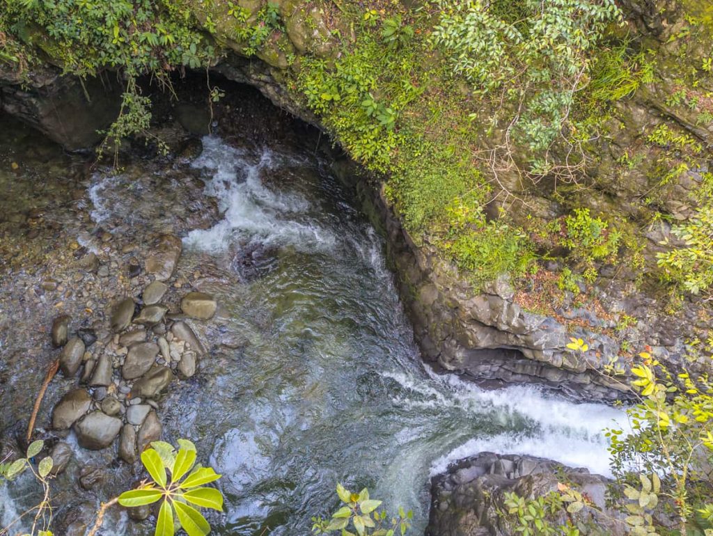 Overhead view of a small stream with clear water rushing through rocks and dense vegetation along the Ruta de las Cascadas in Baños, Ecuador.
