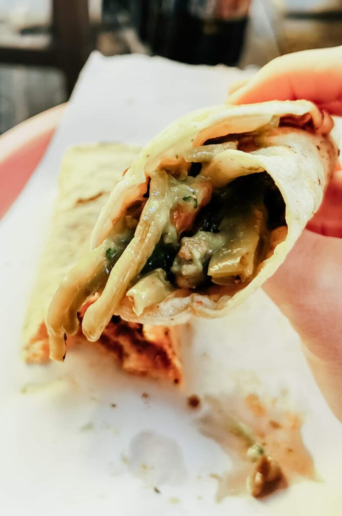 A hand holds up a taco to taste during a taco tour in Mexico City. The corn tortilla is filled with meat and nopal cactus.