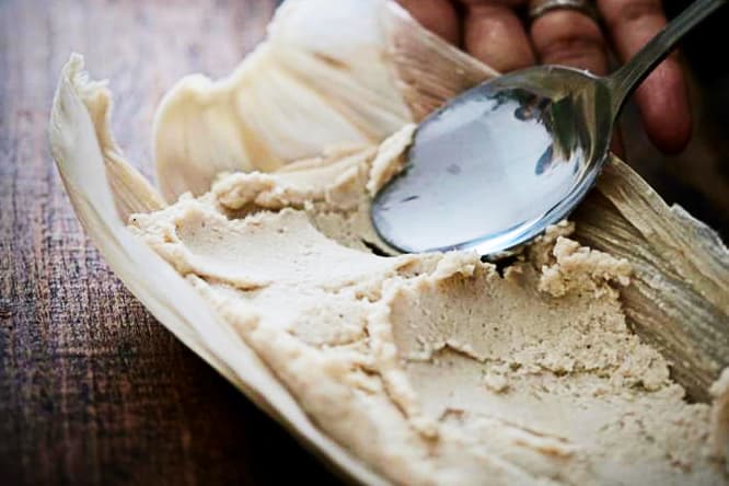 Fingers brace the corn husk as a spoon spreads the masa (corn dough) to make tamales during a cooking class Mexico City.