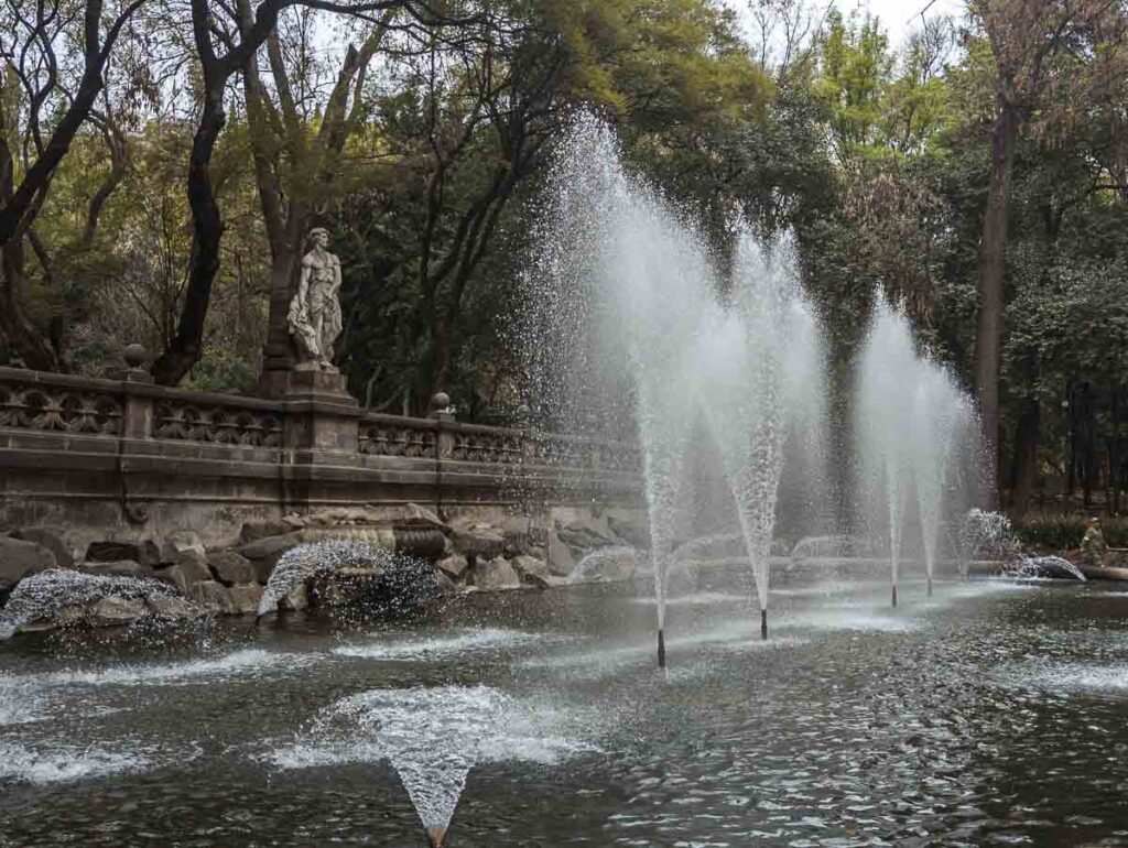 A statue centers the Templanza Fountain in Chapultepec Park Mexico City, surrounded by trees and showcasing the serene beauty of the park.