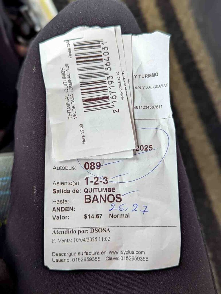 The Baños bus ticket - a white slip of paper with the date, cost, and seat number. Stapled on top are three smaller pieces of paper providing luggage claim.