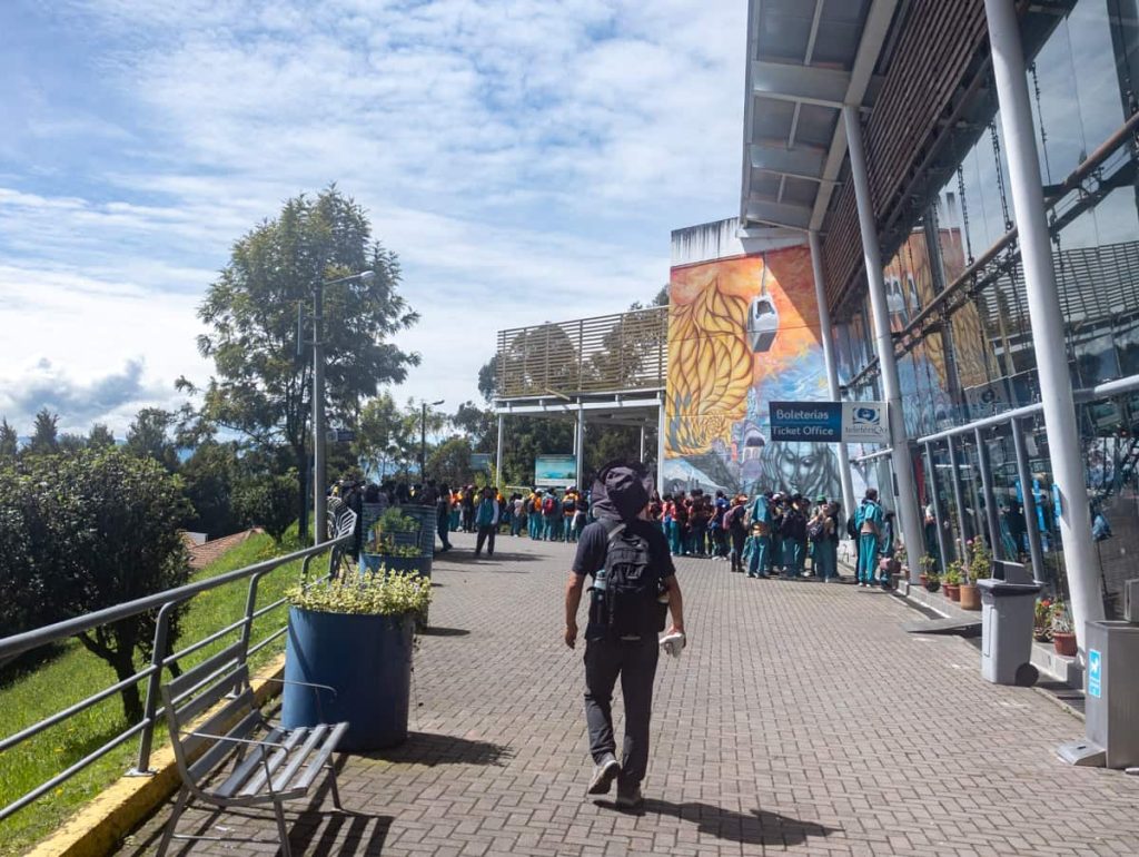 Visitors line up outside the modern glass-walled ticket office for the cable car in Quito Ecuador, with colorful murals decorating the building’s exterior.