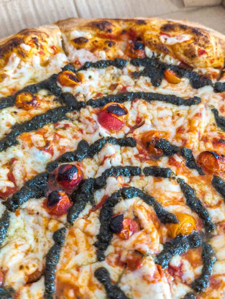 A close up of vegan pizza in Mexico City. The pizza is topped with cherry tomatoes, vegan cheese, and swirled with pesto.
