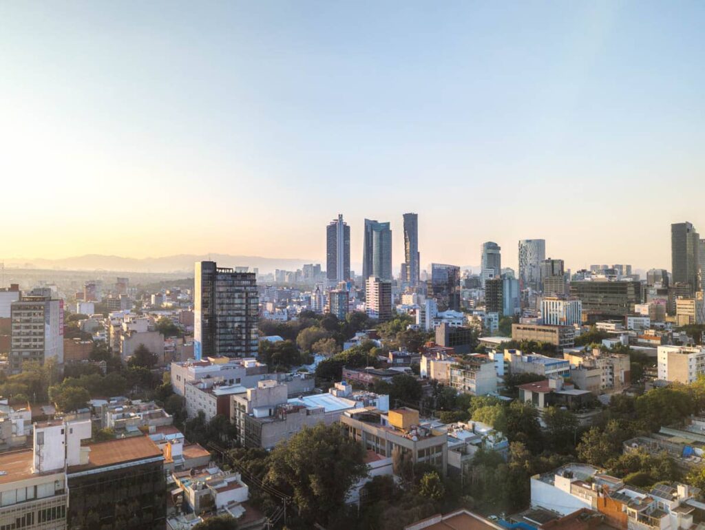View of the Mexico City skyline from Supra Rooftop Bar features tall sky scrapers, small buildings, and mountains in the background.