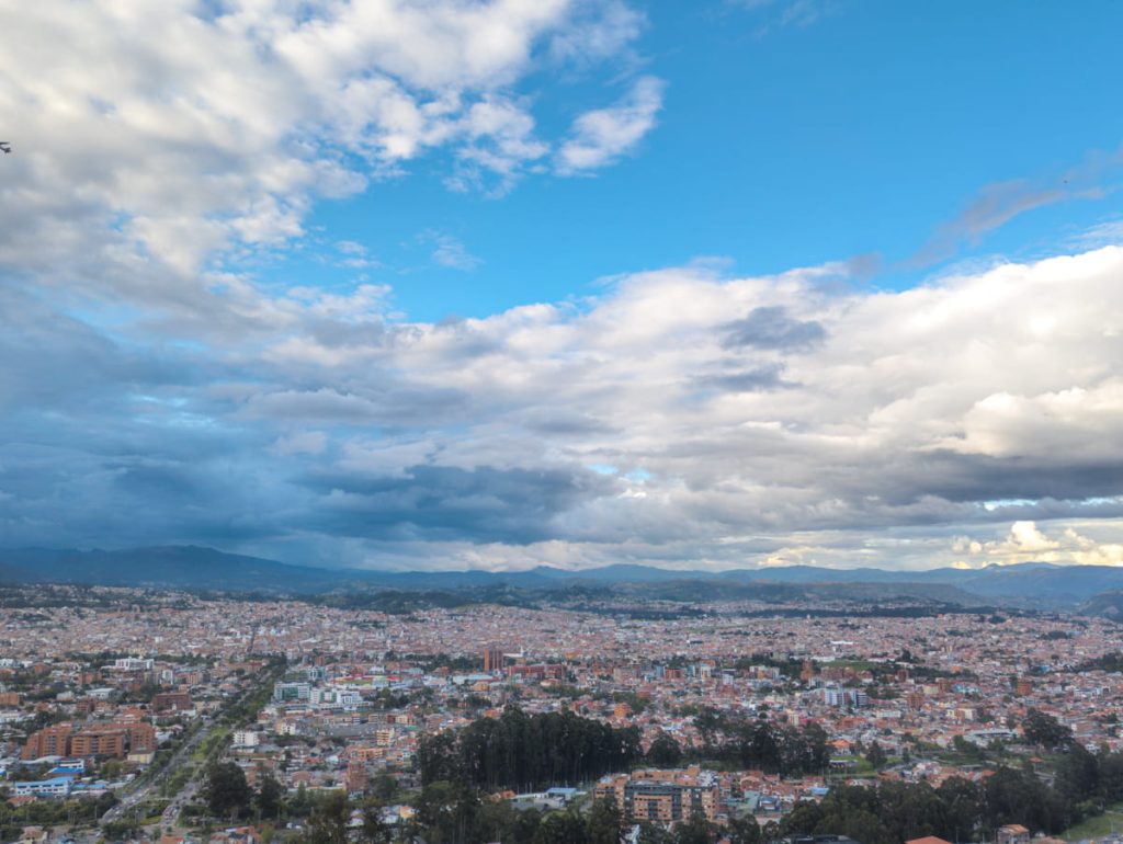 Expansive view of Cuenca Ecuador from El Turi overlook, showing the city’s dense rooftops stretching to the surrounding mountains under a dramatic sky.