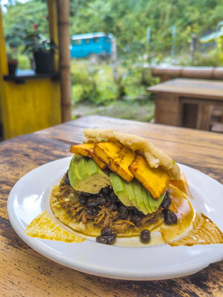 An arepa stuffed with shredded beef, beans, avocado, and fried plantains on a white plate at one of the best places to eat in Mindo Ecuador.