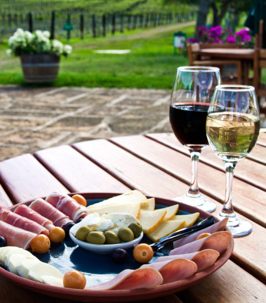 A glass of red wine, a glass of white wine, and a charcuterie plate of cured meats, cheese, and olives on a table at Vinedo Ain Karim.